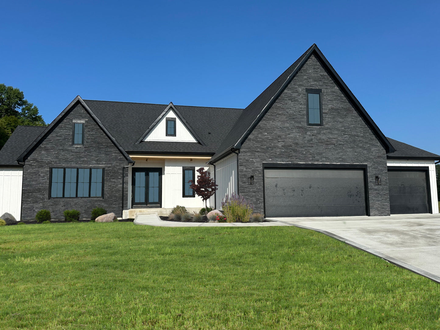 Modern house with gray brick exterior and black roof against a clear blue sky.