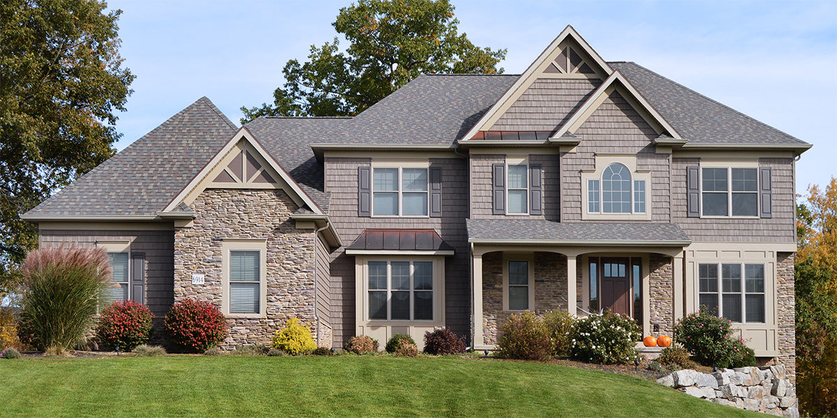 Two-story house with stone and wood exterior, surrounded by greenery.