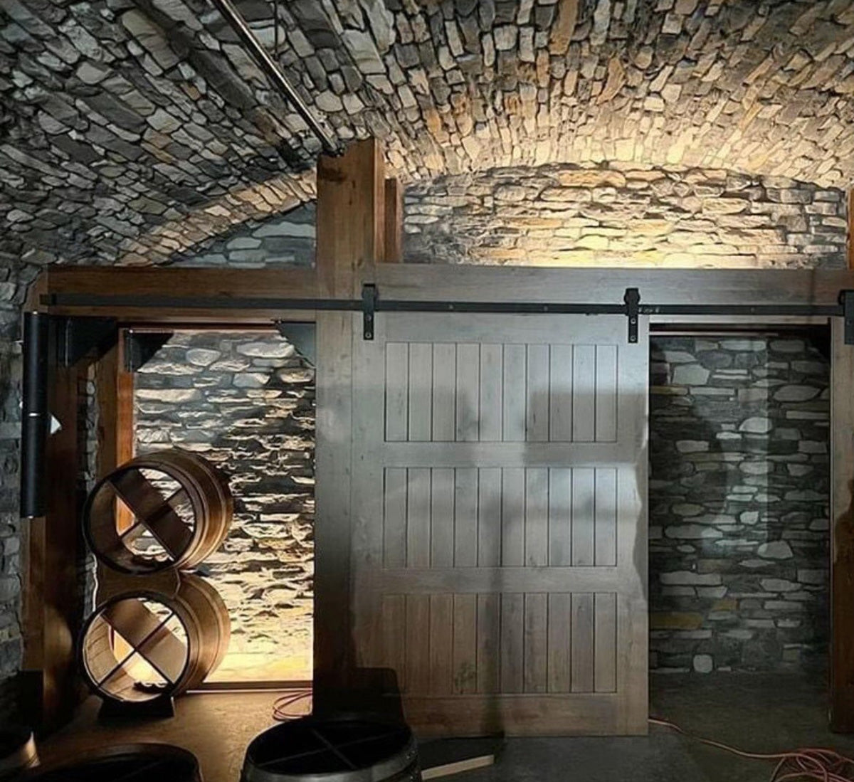 Wooden sliding door in a stone-walled room with stone walls and wooden barrels.