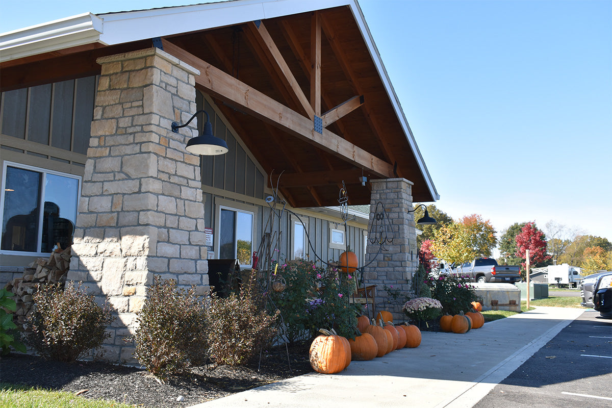 Building exterior with stone facade and wooden overhang, surrounded by pumpkins and autumn foliage.