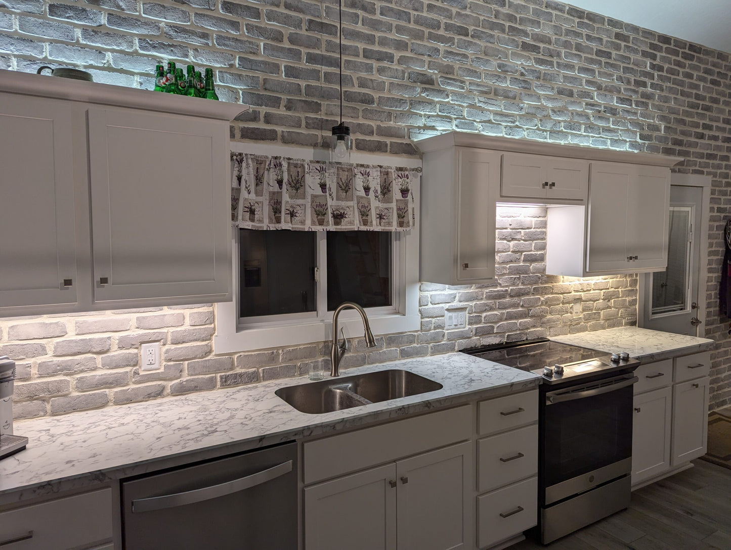 Modern kitchen with gray brick wall, white cabinets, and stainless steel appliances.
