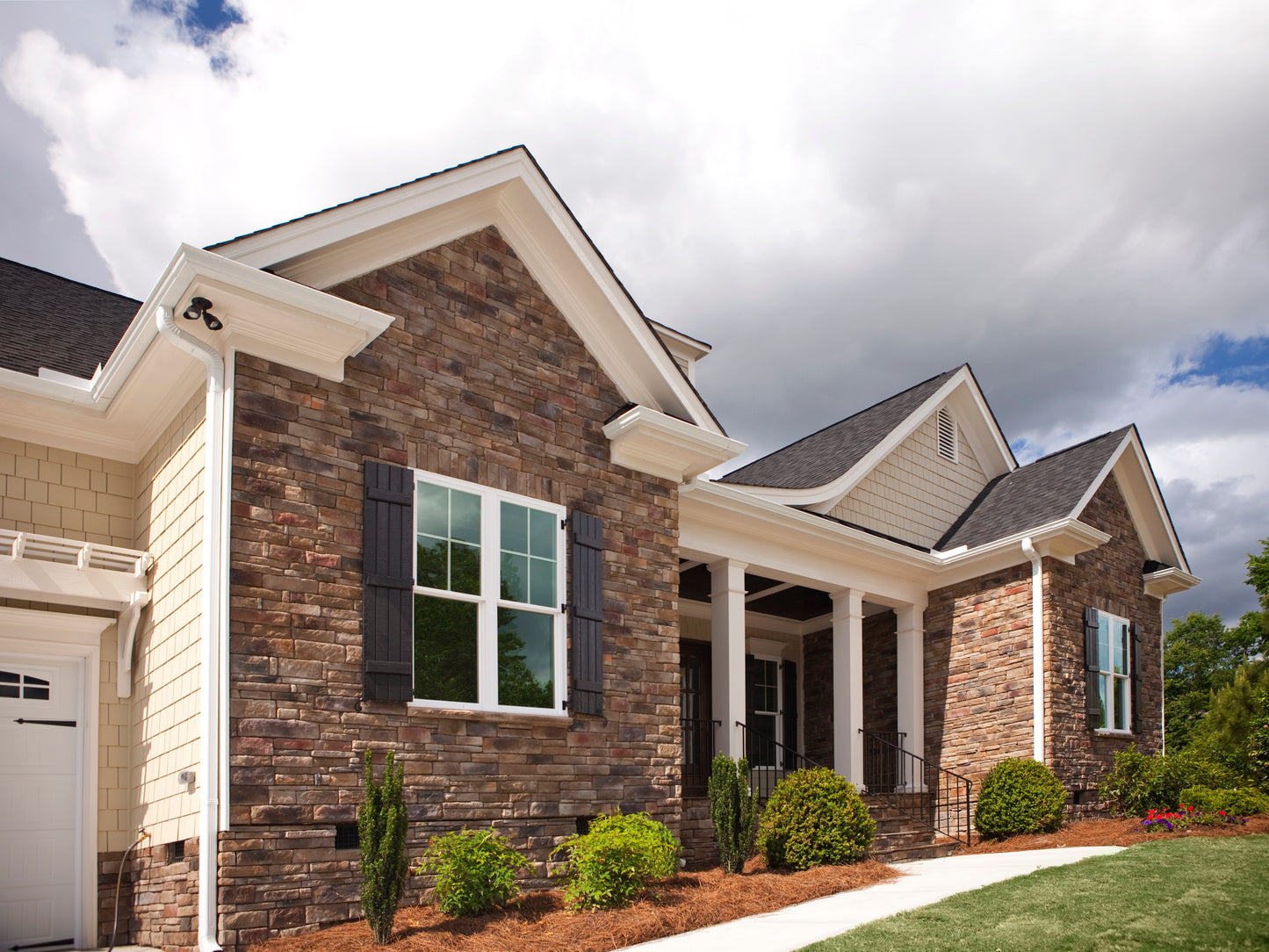 Two-story house with brick facade and white trim under a cloudy sky.