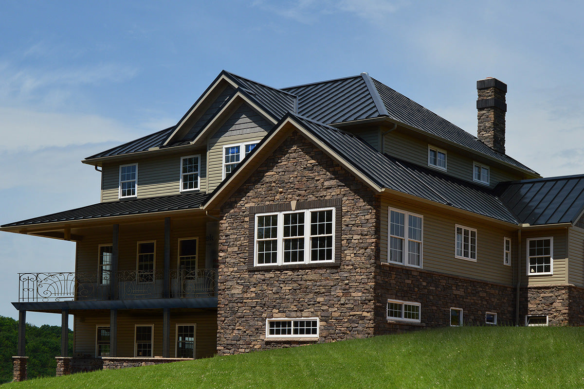 Two-story house with stone facade and metal roof against a blue sky.
