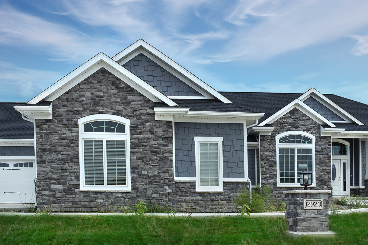 Two-story house with gray stone facade and white trim against a blue sky.