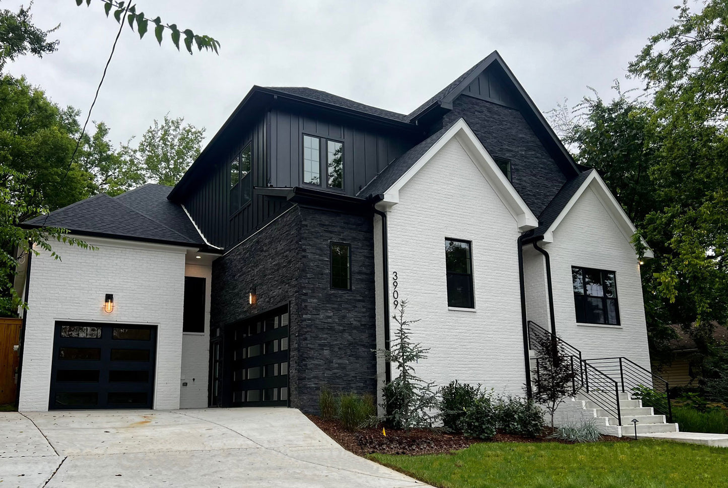 Modern house with white exterior and dark roof, surrounded by trees.