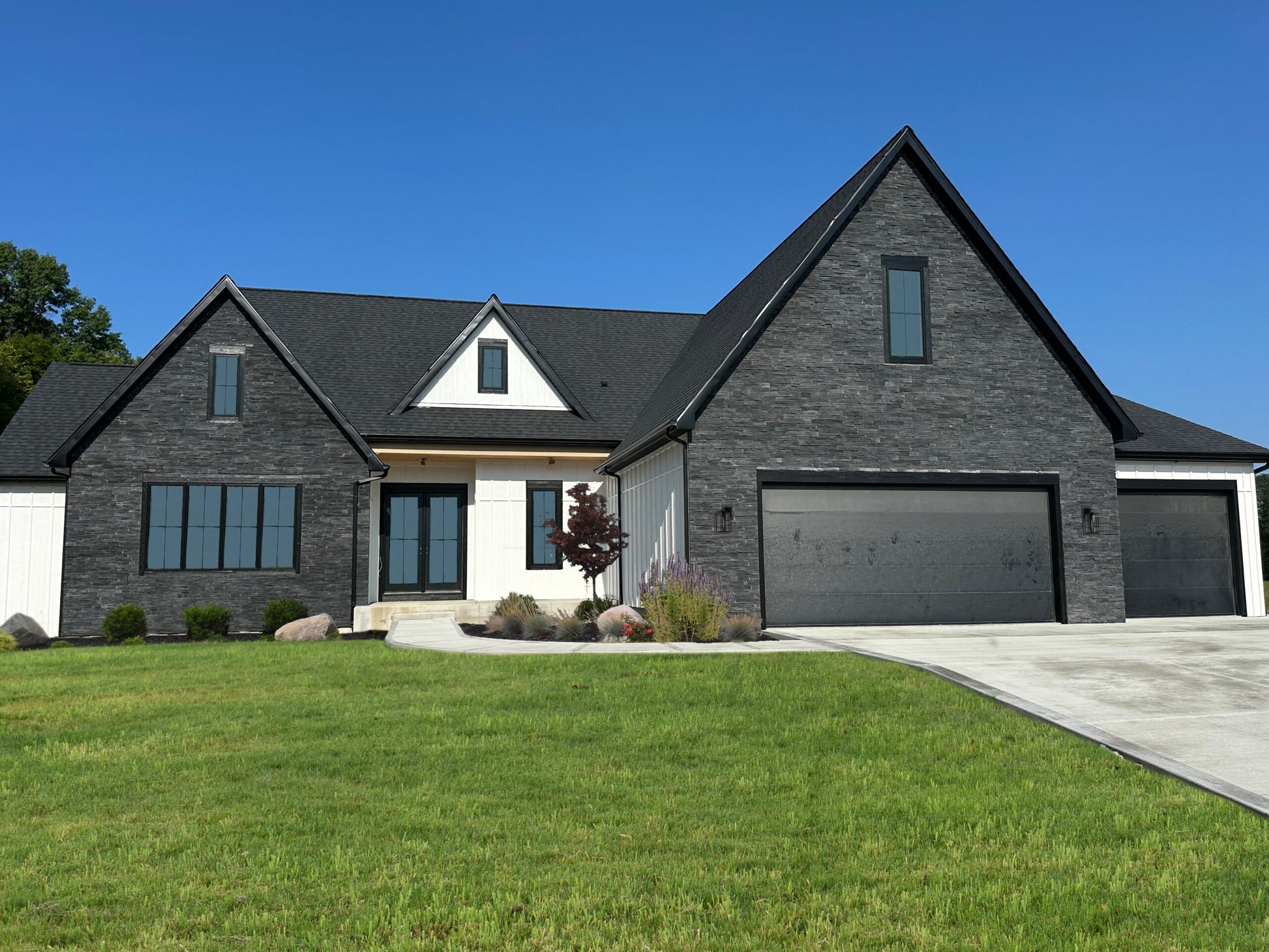 Modern house with gray brick exterior and black roof against a clear blue sky.