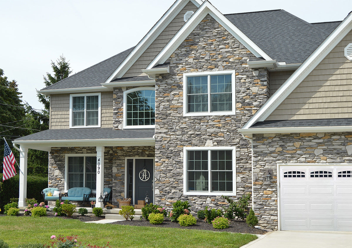 Two-story house with stone facade and white garage door, featuring an American flag.