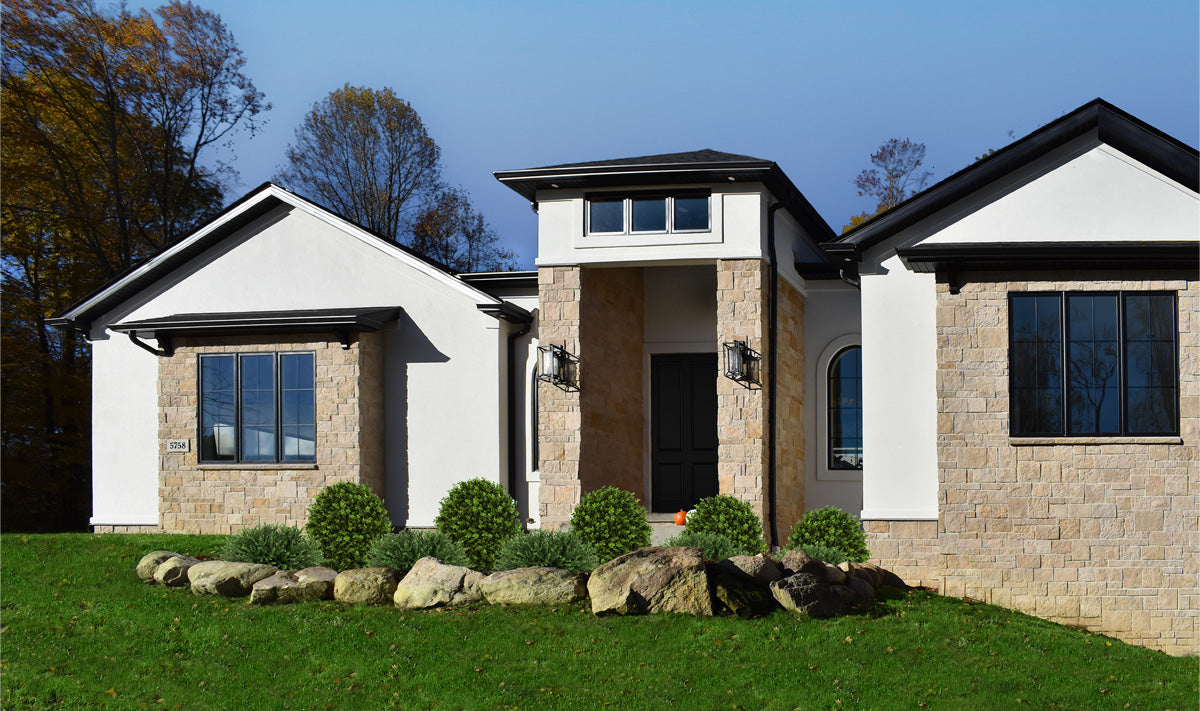 Modern house with white exterior and stone accents, surrounded by greenery.
