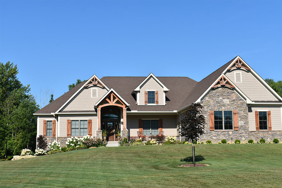 Two-story house with a gray exterior and brown roof, surrounded by green grass and trees.