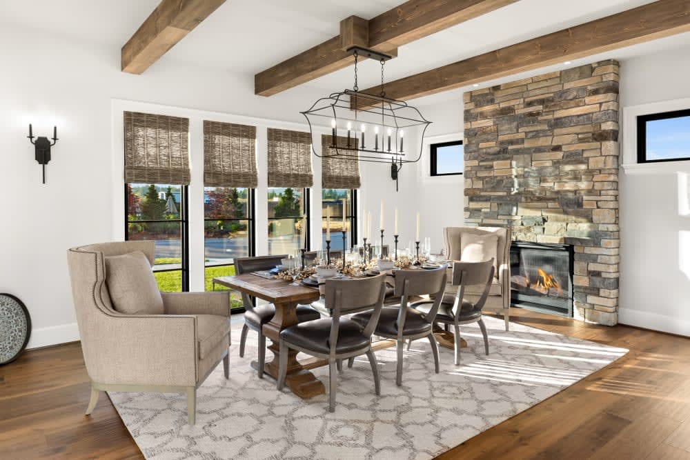 Earth-toned ledgestone fireplace wall beside a bright dining room and wood ceiling beams, featuring Cultured Stone Echo Ridge Country Ledgestone.