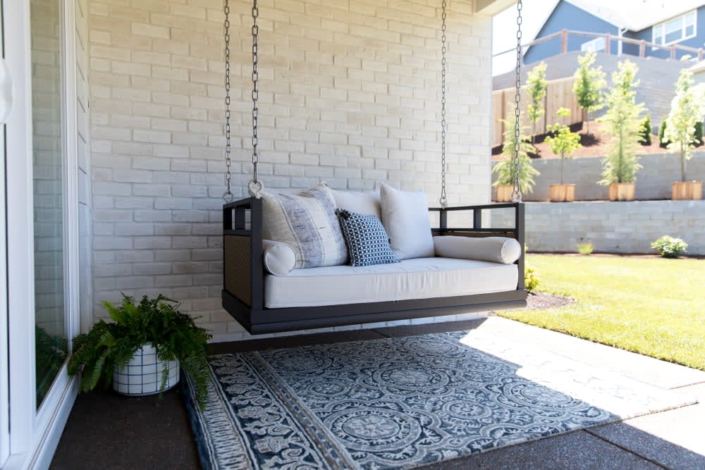 White handmade brick porch wall behind a suspended upholstered swing, featuring Cultured Stone Canvas Unpainted Handmade Brick.
