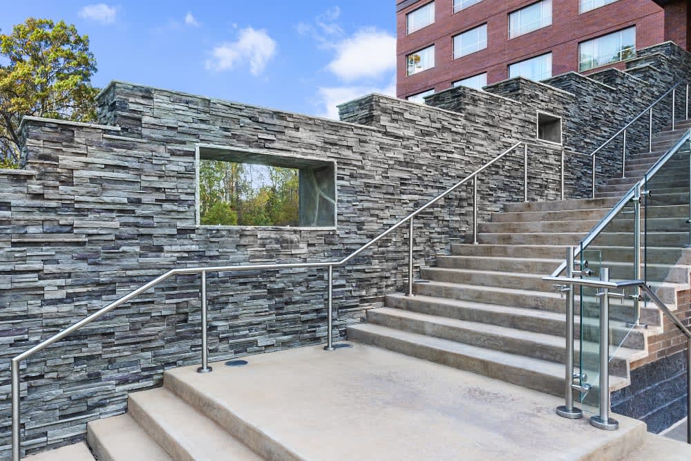 Dark linear stone walls beside a wide outdoor staircase with metal railings, featuring Cultured Stone Black Mountain Pro-Fit Alpine Ledgestone.