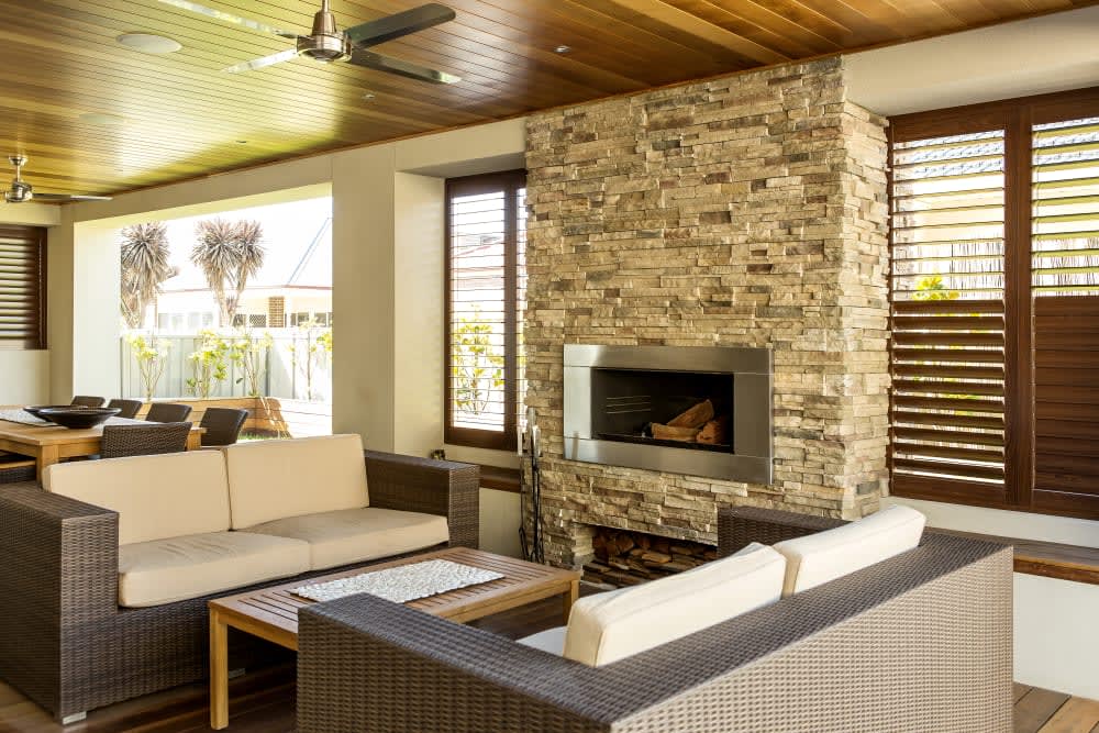 Warm ledgestone fireplace in a wood-ceilinged sitting room with woven lounge furniture, featuring Cultured Stone Chardonnay Pro-Fit Alpine Ledgestone.