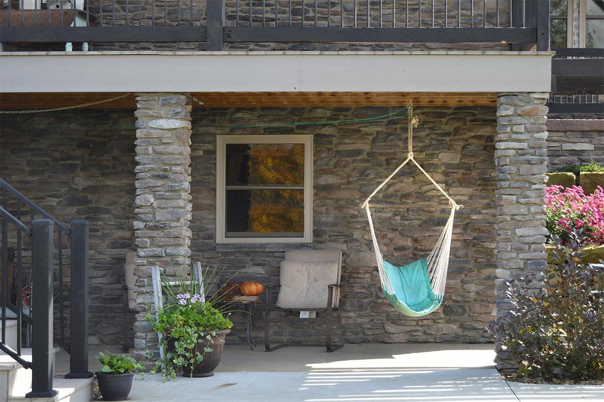 Turquoise hammock chair hanging from a wooden swing set against a stone wall.