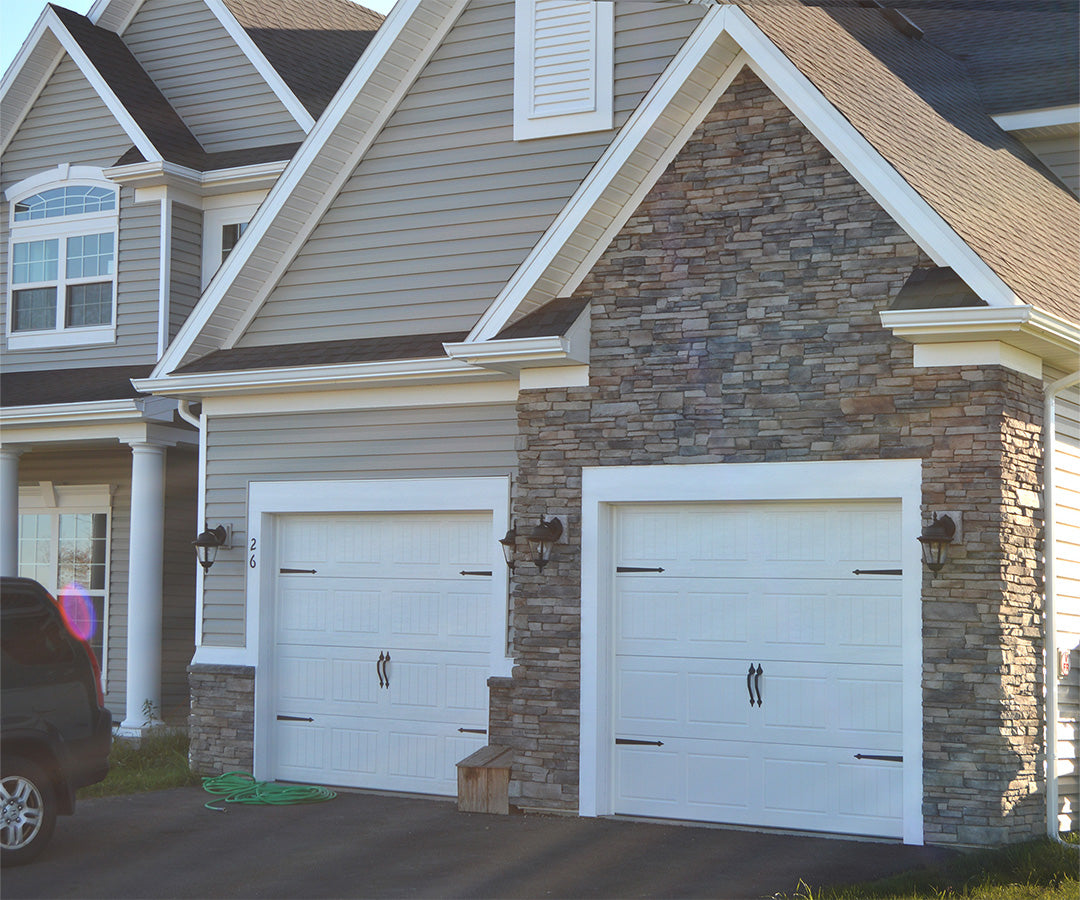 Two white garage doors on a house with stone facade