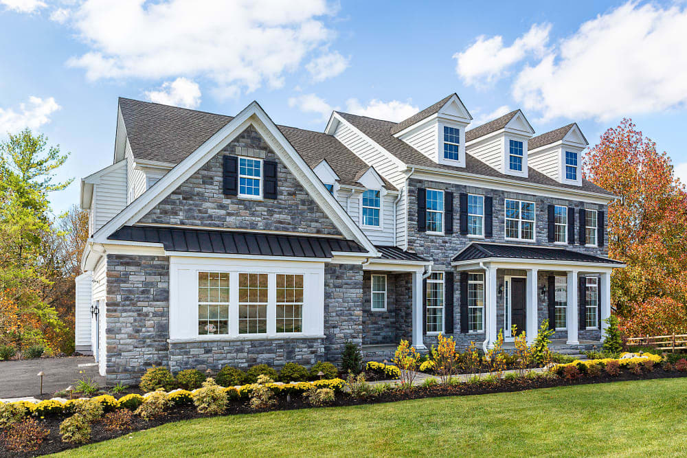Gray limestone facade on a two-story home with a long covered porch and autumn planting, featuring Dutch Quality Elkwood Limestone.