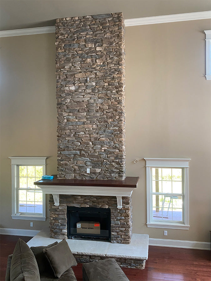 Stone fireplace in a living room with two windows and a couch.
