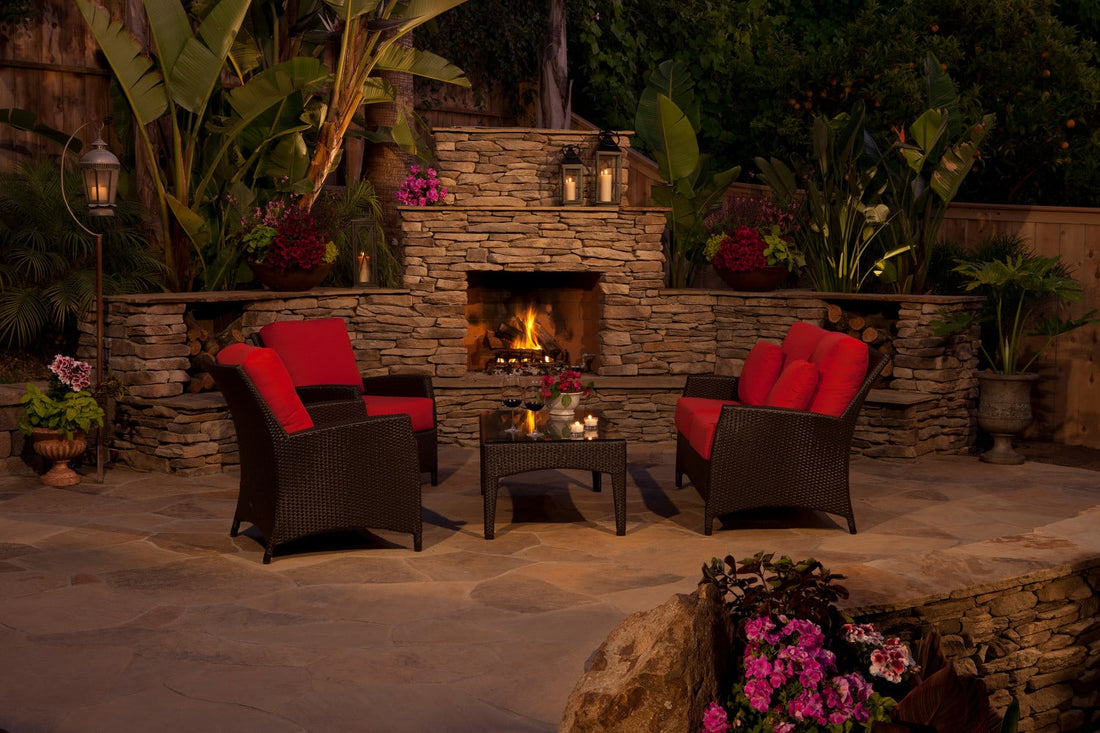 Ledgestone outdoor fireplace with red-cushioned seating and lush patio planting, featuring Eldorado Prescott Bluffstone.