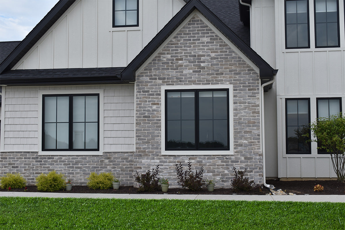 House with gray brick facade and white siding, featuring large windows.