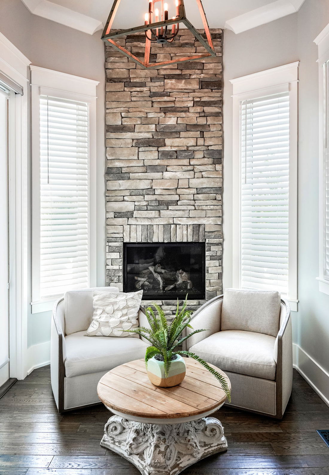 Stone fireplace beneath a chandelier between two white chairs and tall windows, featuring Provia Frost Terra Cut.