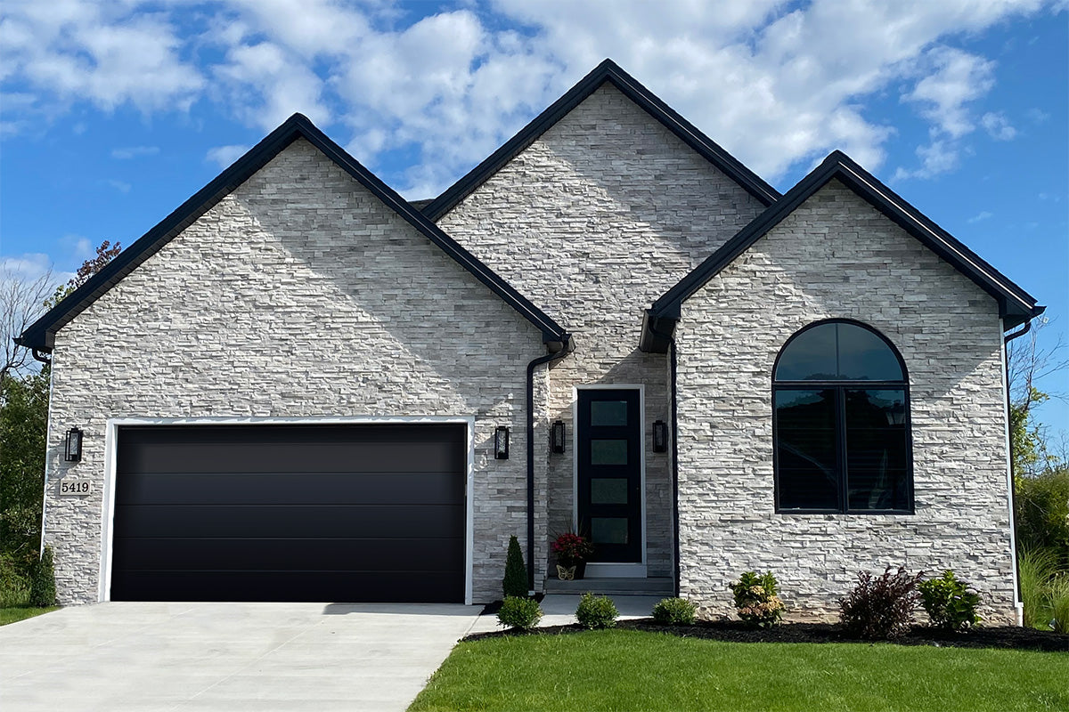 Modern house with stone facade and black garage door under a blue sky.