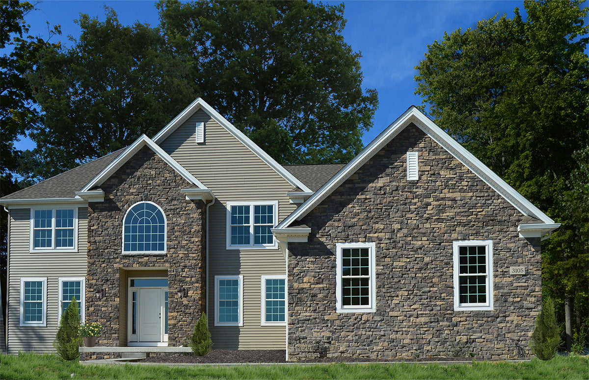 Two-story house with stone facade and gray roof, surrounded by trees.