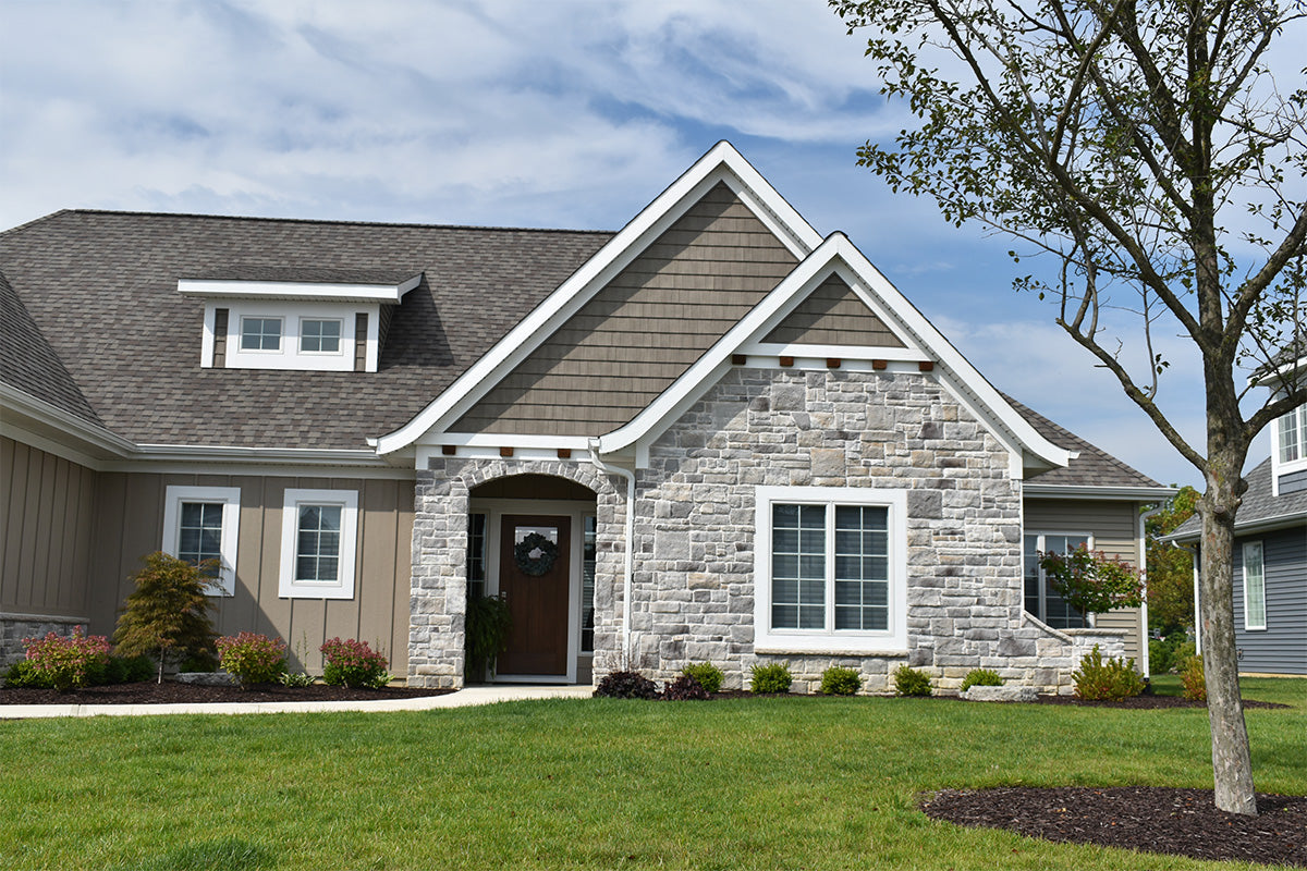 Two-story house with a combination of siding and stone facade, surrounded by green grass and trees.