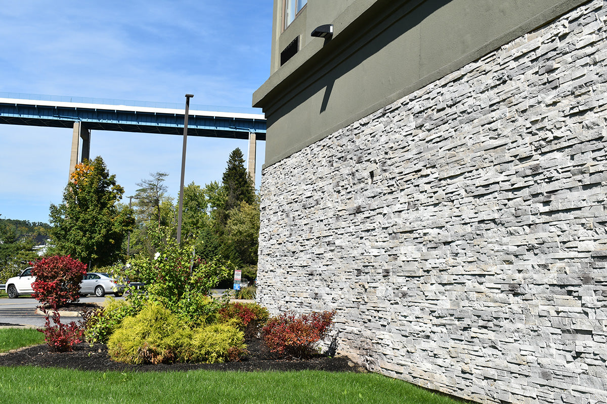Building exterior with stone wall, greenery, and a bridge in the background