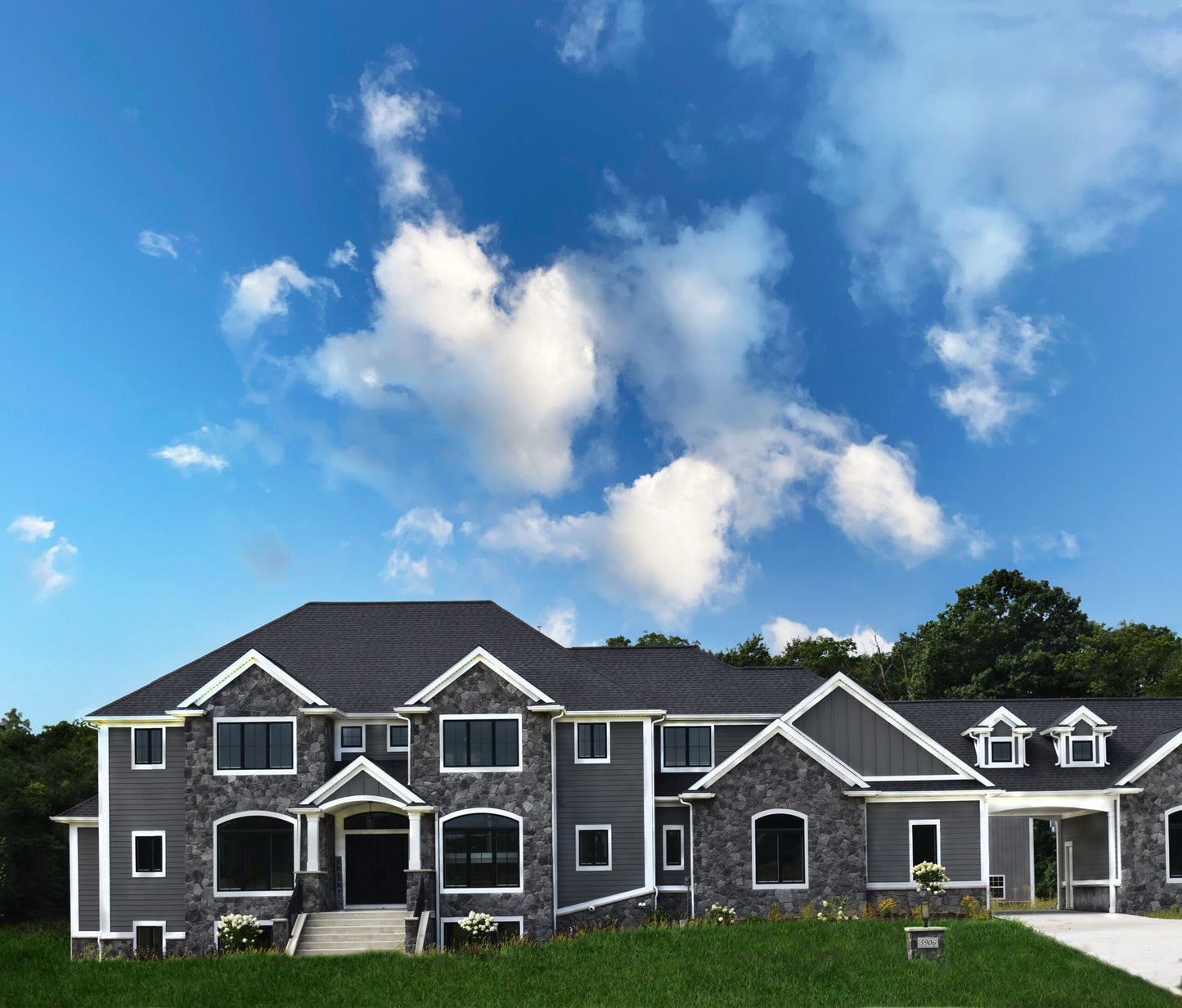 Large house with gray siding and black roof against a blue sky with white clouds