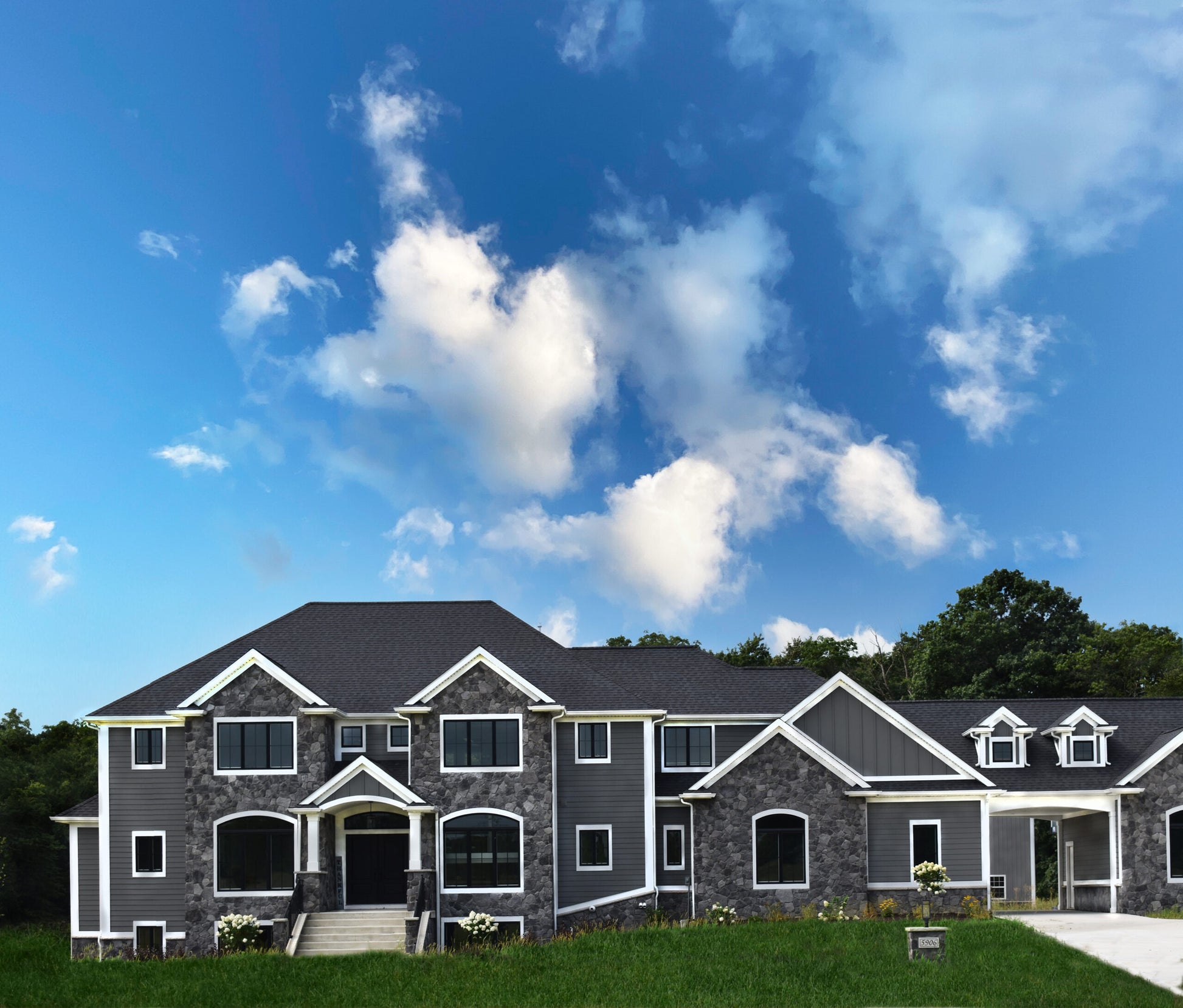 Large house with gray siding and black roof against a blue sky with white clouds
