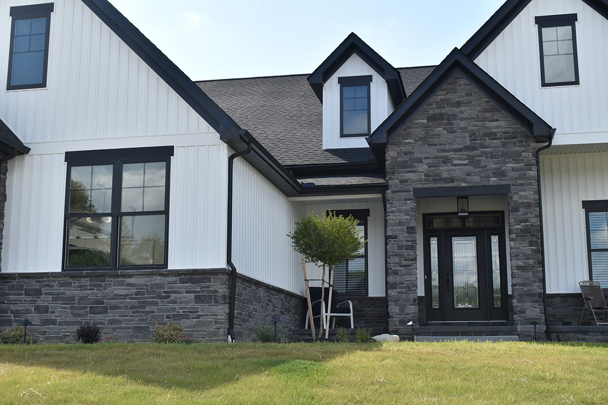 Two-story house with gray stone facade and white siding, featuring a front door and windows.