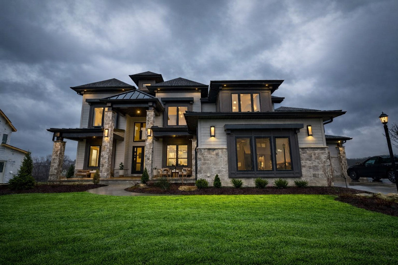Large, luxurious house with illuminated windows on a cloudy evening.