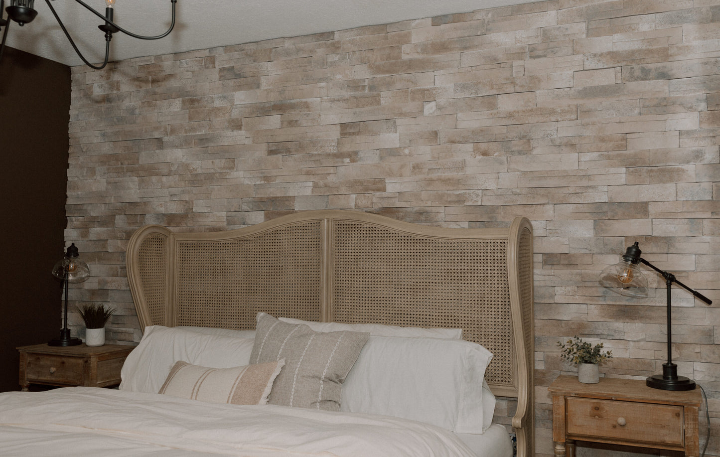 Bedroom with stone wall, bed, and nightstands with lamps.