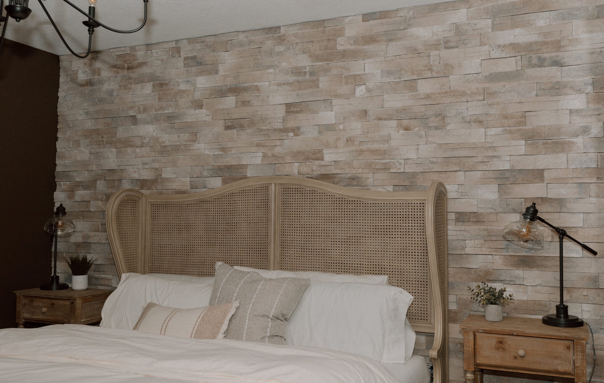 Bedroom with stone wall, bed, and nightstands with lamps.