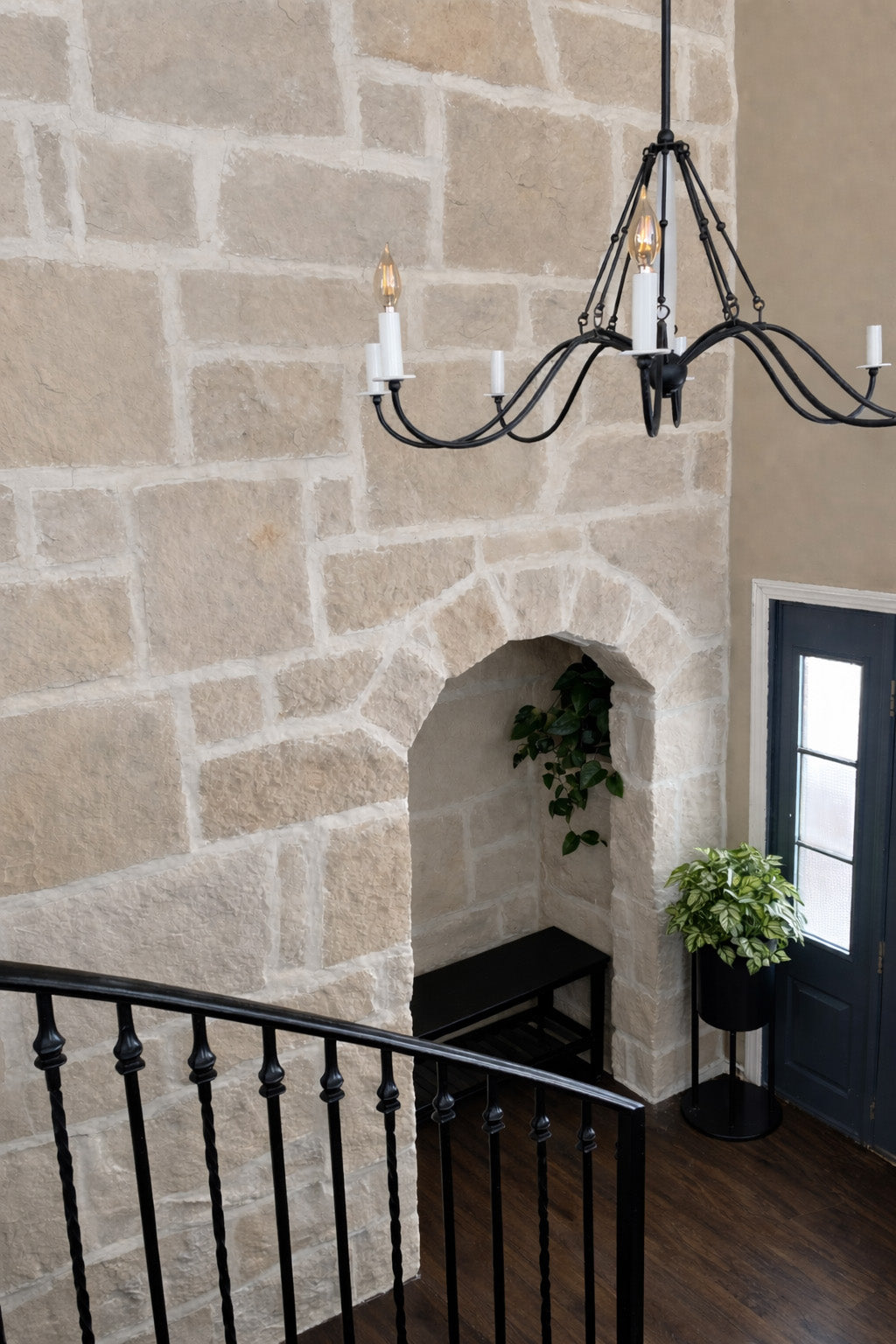 Foyer with stone wall, black chandelier, and decorative plants.