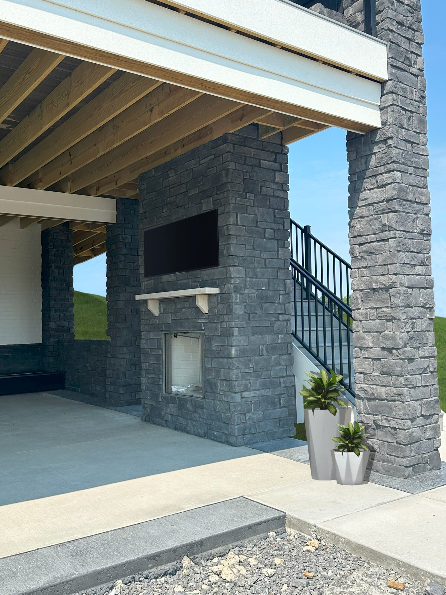 Outdoor patio area with stone wall, TV, and potted plants under a covered deck.