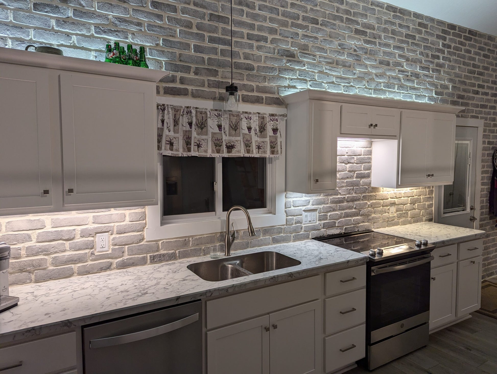 Modern kitchen with gray brick wall, white cabinets, and stainless steel appliances.
