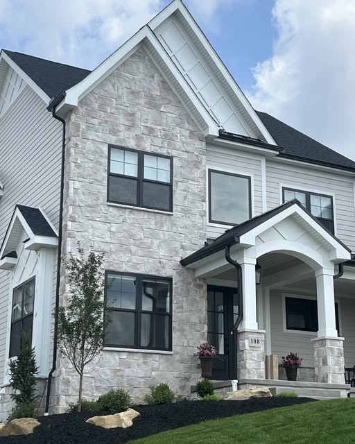 Two-story house with stone facade and black windows under a blue sky.