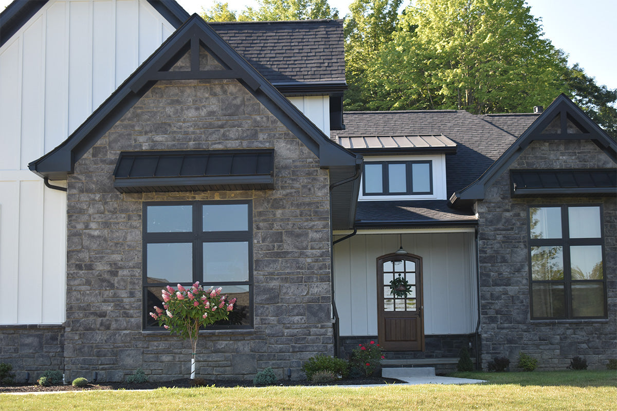 Stylish house with stone facade and black roof, surrounded by greenery.