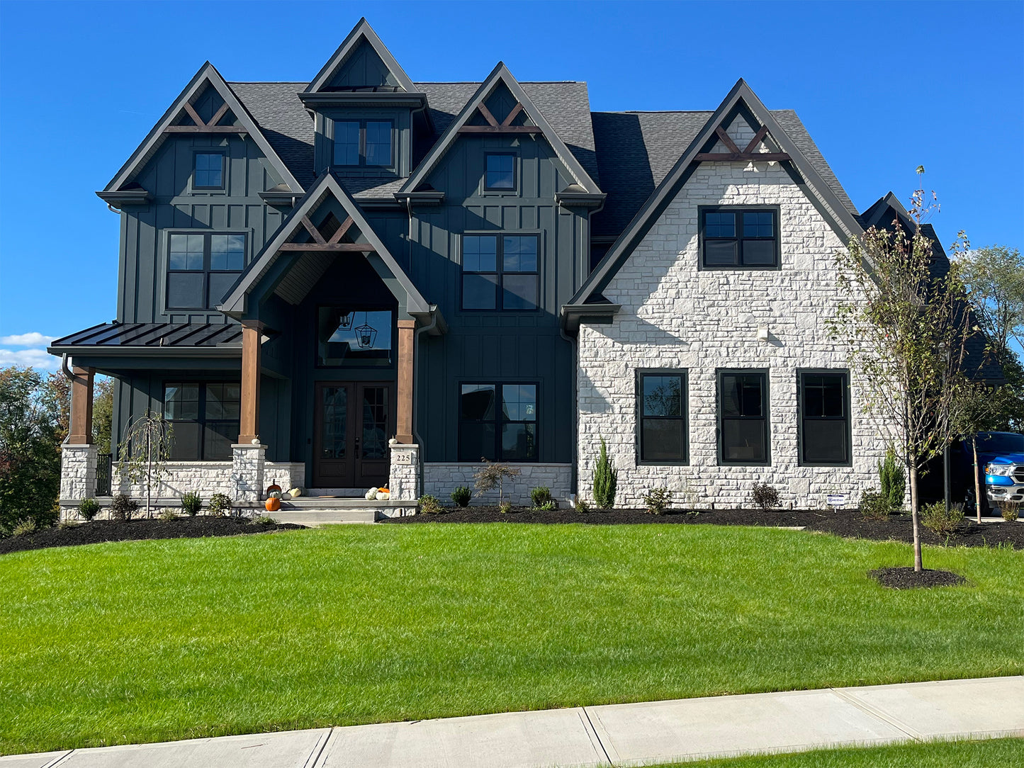Two-story house with dark exterior and light stone accents on a clear day.