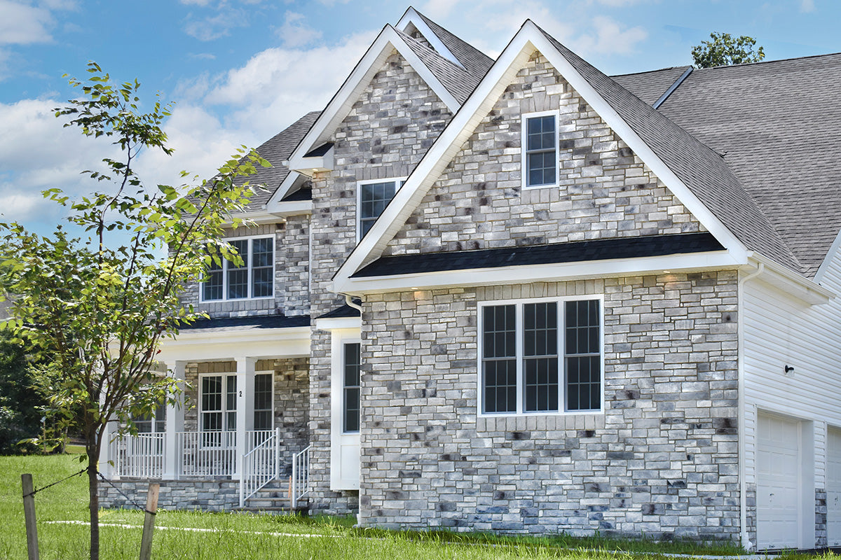 Two-story house with stone facade and white trim on a clear day