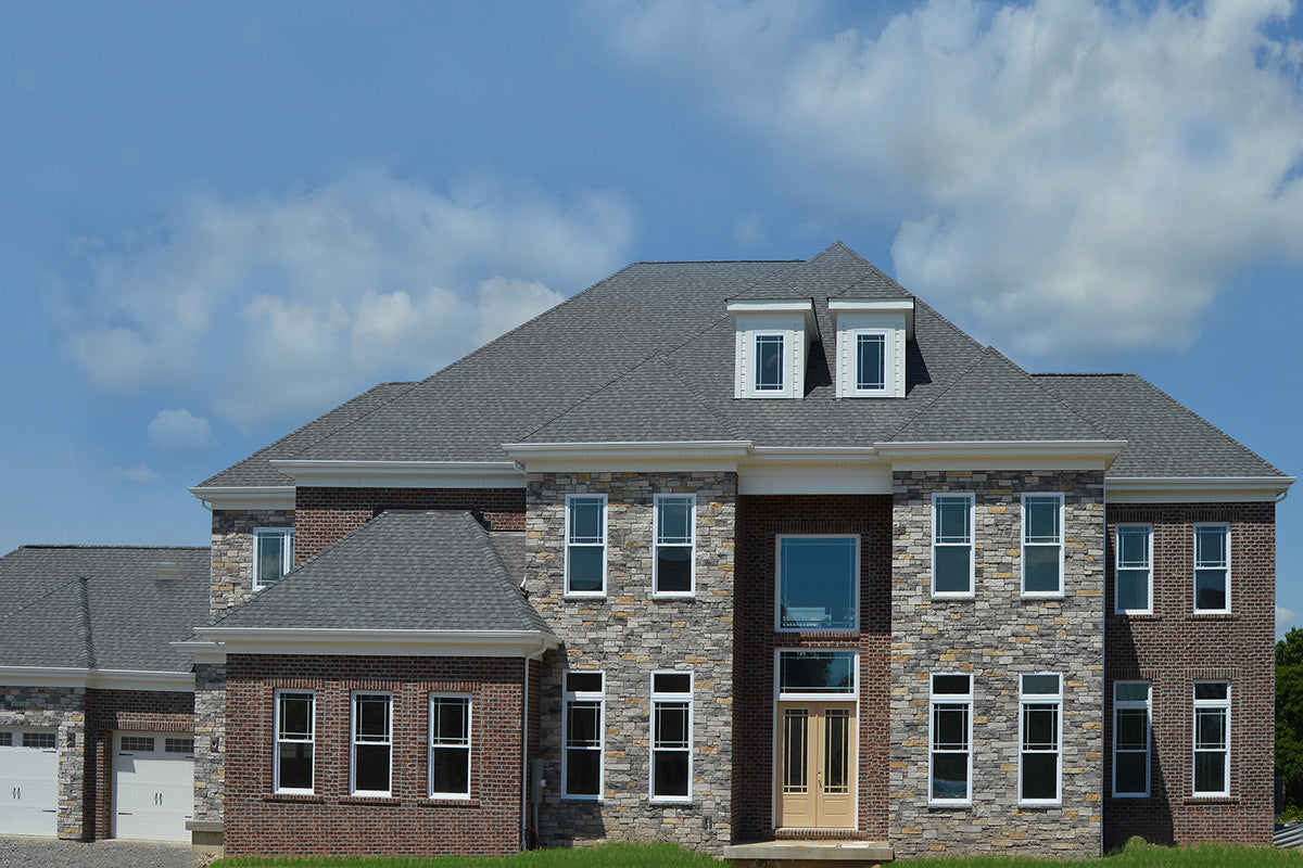 Two-story house with stone and brick facade under a blue sky with clouds.