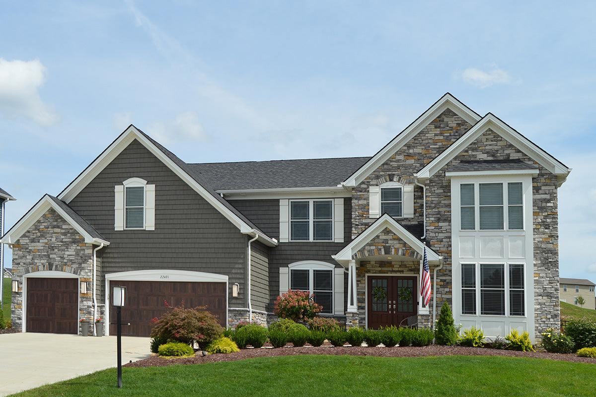 Two-story house with gray siding and stone accents on a clear day.