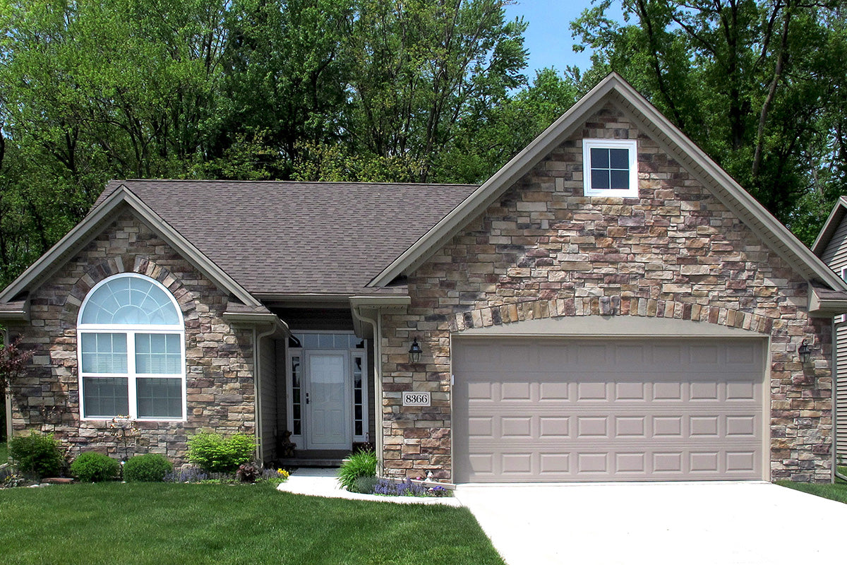 Stone house with a gray roof and white door, surrounded by greenery.