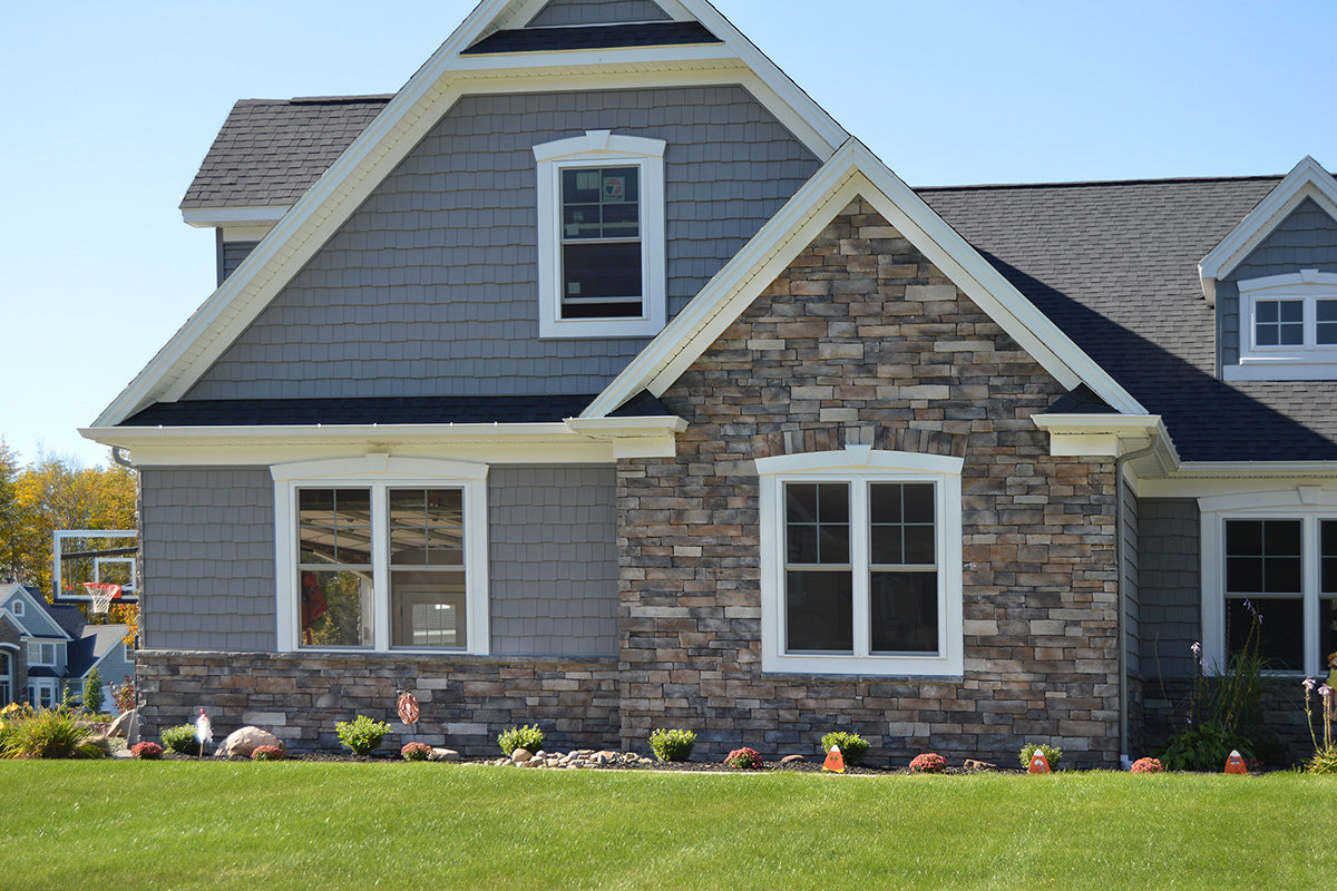 Two-story house with gray siding and stone facade, featuring white windows and gutters.