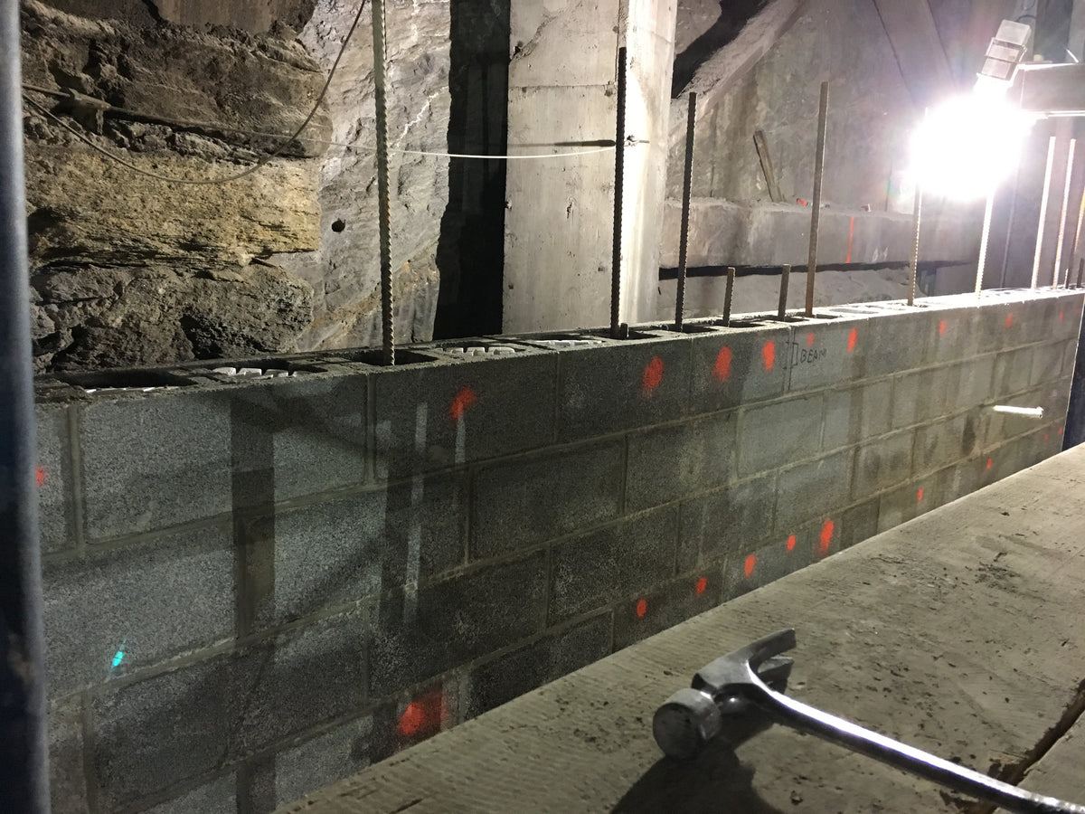 Gray CMU block wall in running bond under construction, with reinforcement extending above the top course.