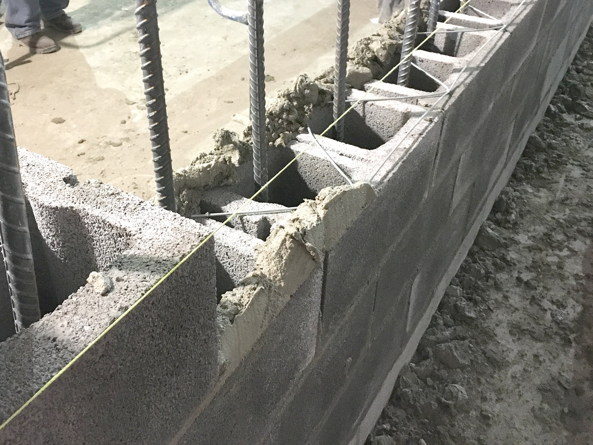 Concrete masonry wall under construction with open cores, vertical rebar and horizontal joint reinforcement.
