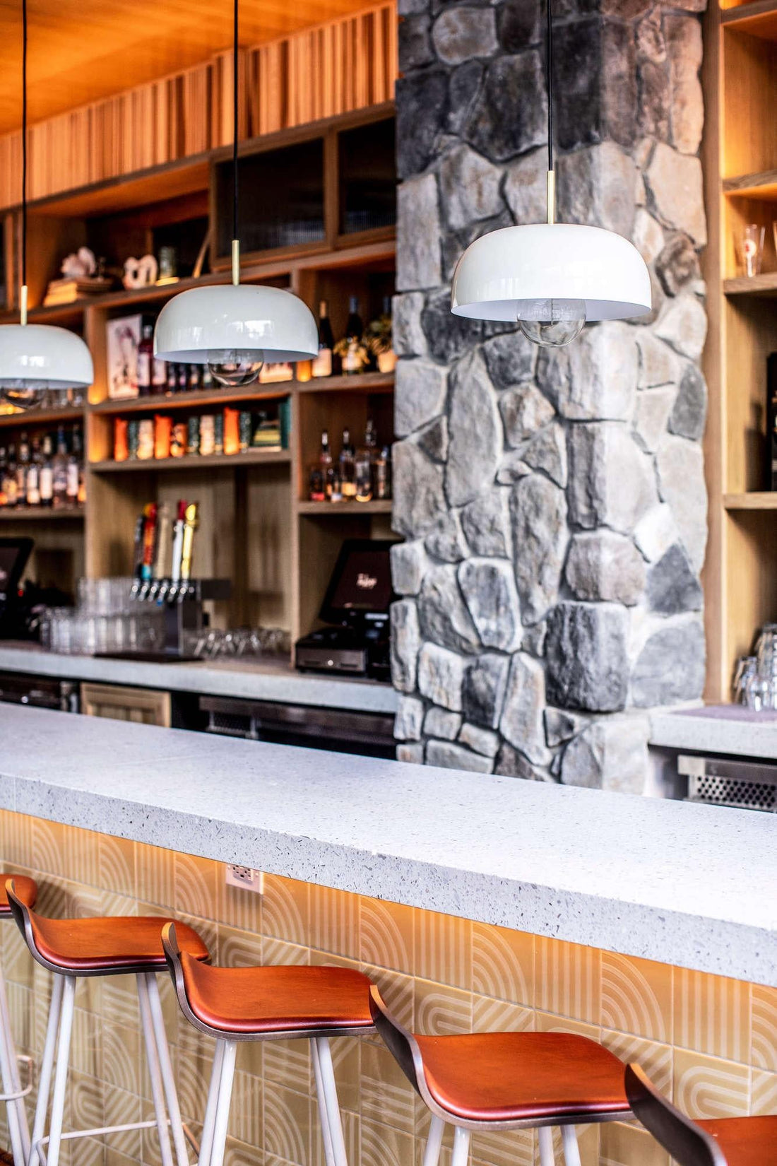 Gray fieldstone column beside a bar with pendant lights and leather stools, featuring Cultured Stone Echo Ridge Dressed Fieldstone.