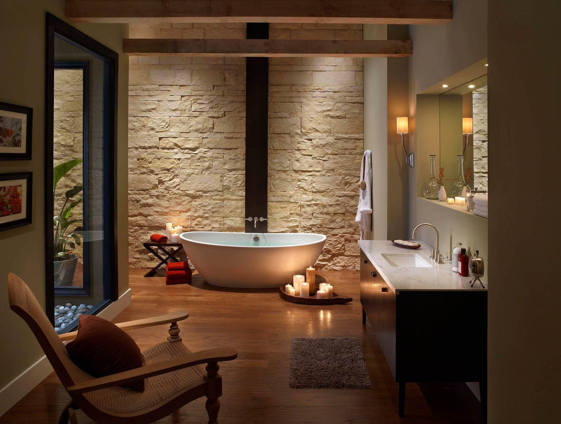 Cream stone wall behind a freestanding bathtub in a warmly lit bathroom, featuring Eldorado Oyster Cut Coarse Stone.