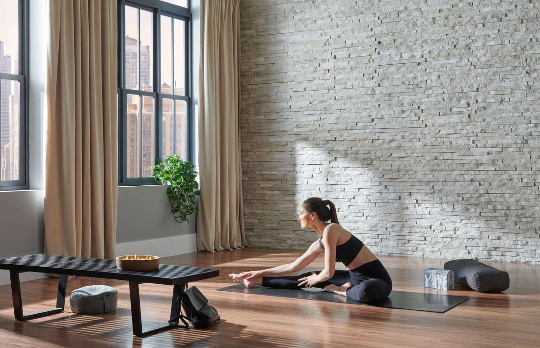 Pale linear stone accent wall in a bright wood-floored exercise space, featuring Eldorado Sea Cliff European Ledge.